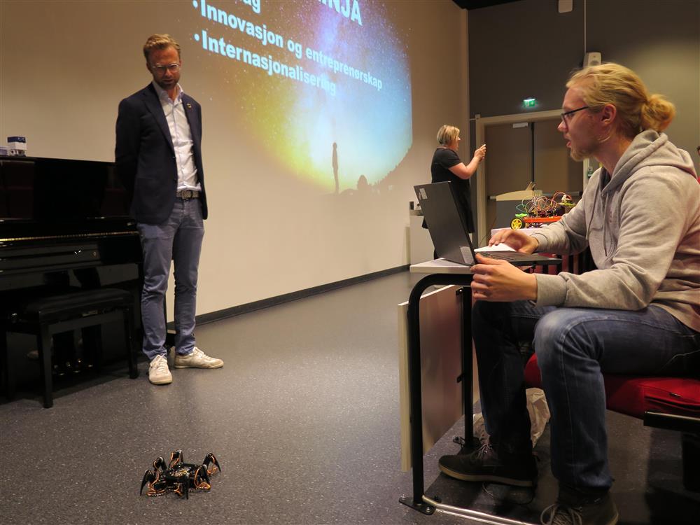Digitaliseringsminister Nikolai Astrup som ser på at en elev styrer en robot - Klikk for stort bilde
