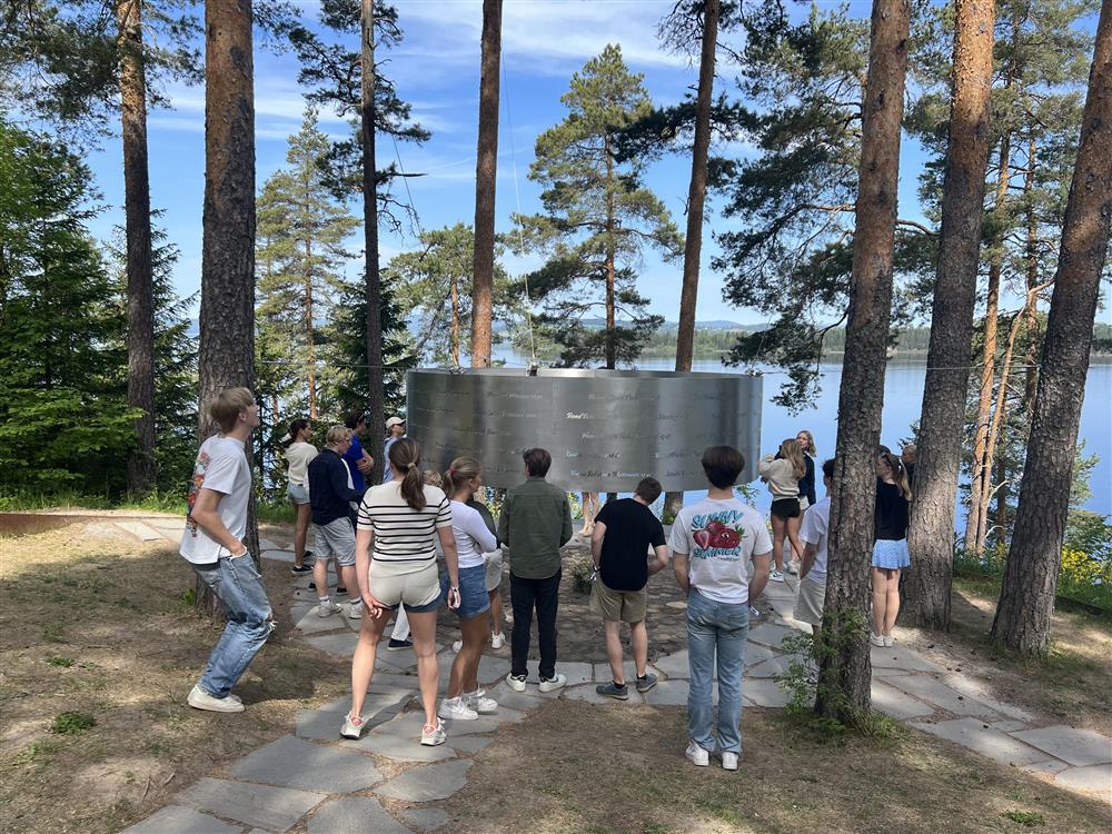 Flere ungdommer står blant trærne og leser navn på et minnesmerke - Klikk for stort bilde