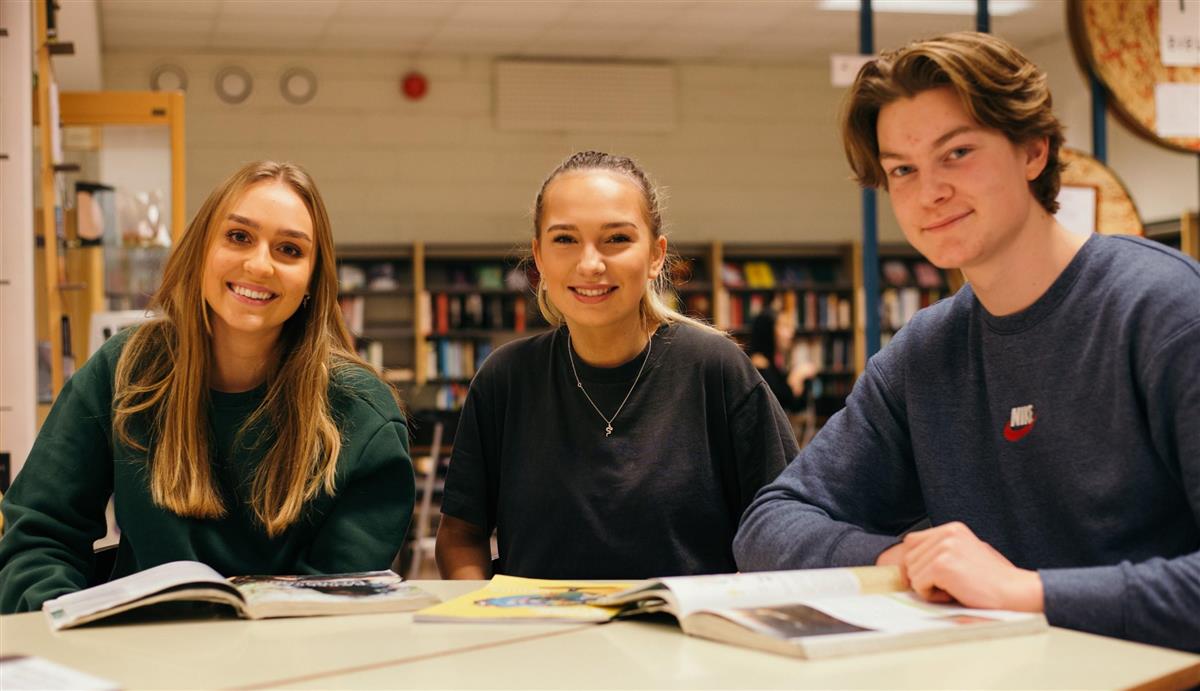 Tre elever sitter rundt et bord på biblioteket - Klikk for stort bilde