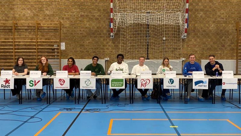 Ungdomspolitikere med sine partiers logoer deltar i skoledebatt i forbindelse med kommune- og fylkestingsvalget 2023. - Klikk for stort bilde