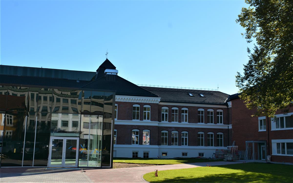 Skolebygget med kantinedel og den eldste delen av skolen, med grønt gress foran. - Klikk for stort bilde