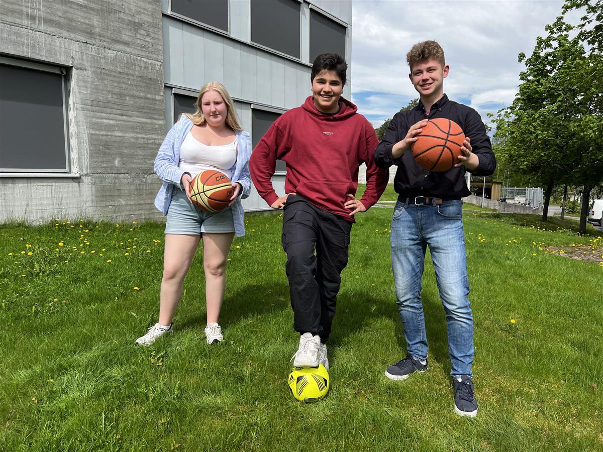 Tre elever står på en gressplen med basketballer og fotballer. - Klikk for stort bilde