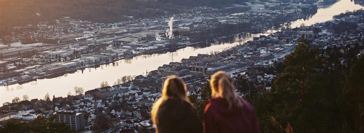 To jenter ser ut over byen, en elv renner i midten - Klikk for stort bilde