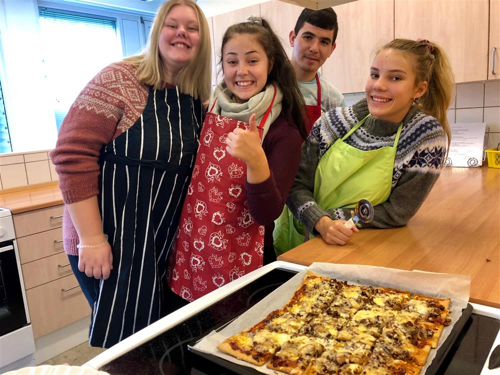 Tre jenter og en gutt som lager pizza på skolekjøkkenet - Klikk for stort bilde