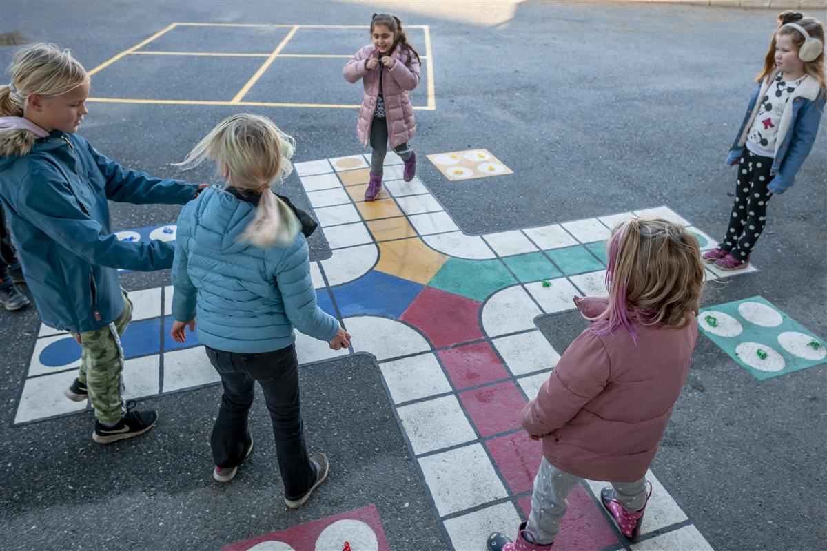 Barn driver fysisk aktiv læring i oppmerket område i skolegård.  - Klikk for stort bilde
