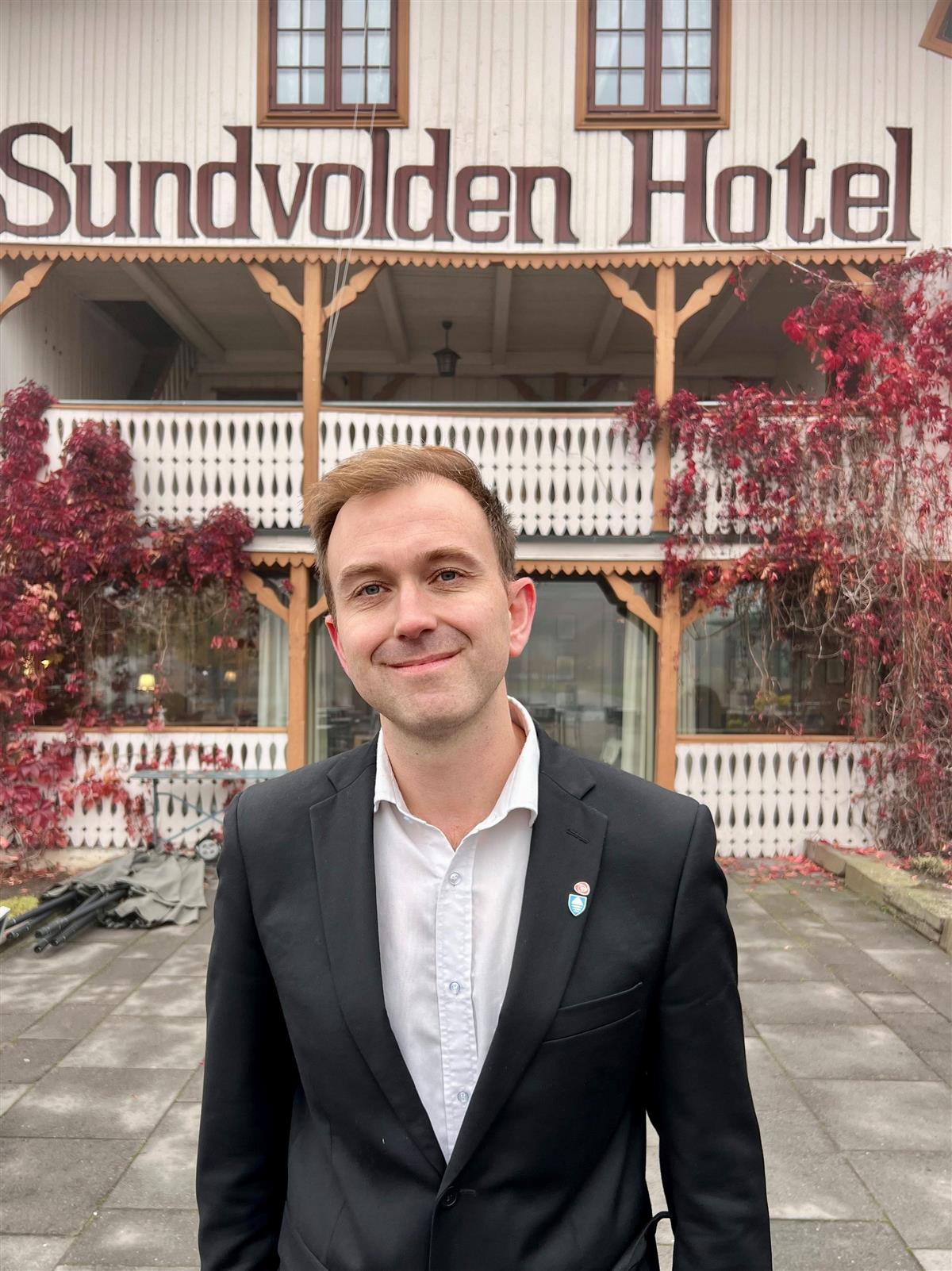 Edvin Søvik i dress står foran inngangen til et hotellbygg - Klikk for stort bilde