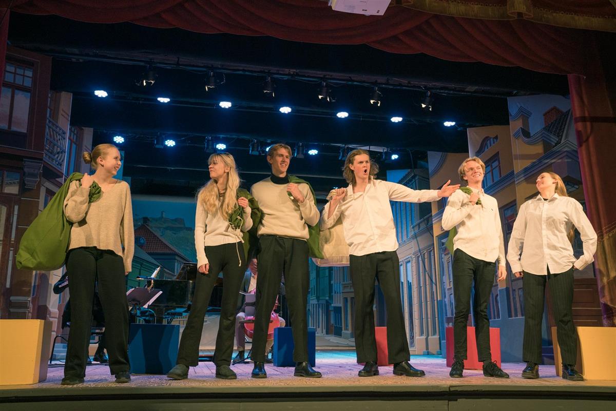 De seks musikkelevene på scenen kledd i hvite gensere og svarte bukser. Tre av dem holder en grønn tøypose.  - Klikk for stort bilde
