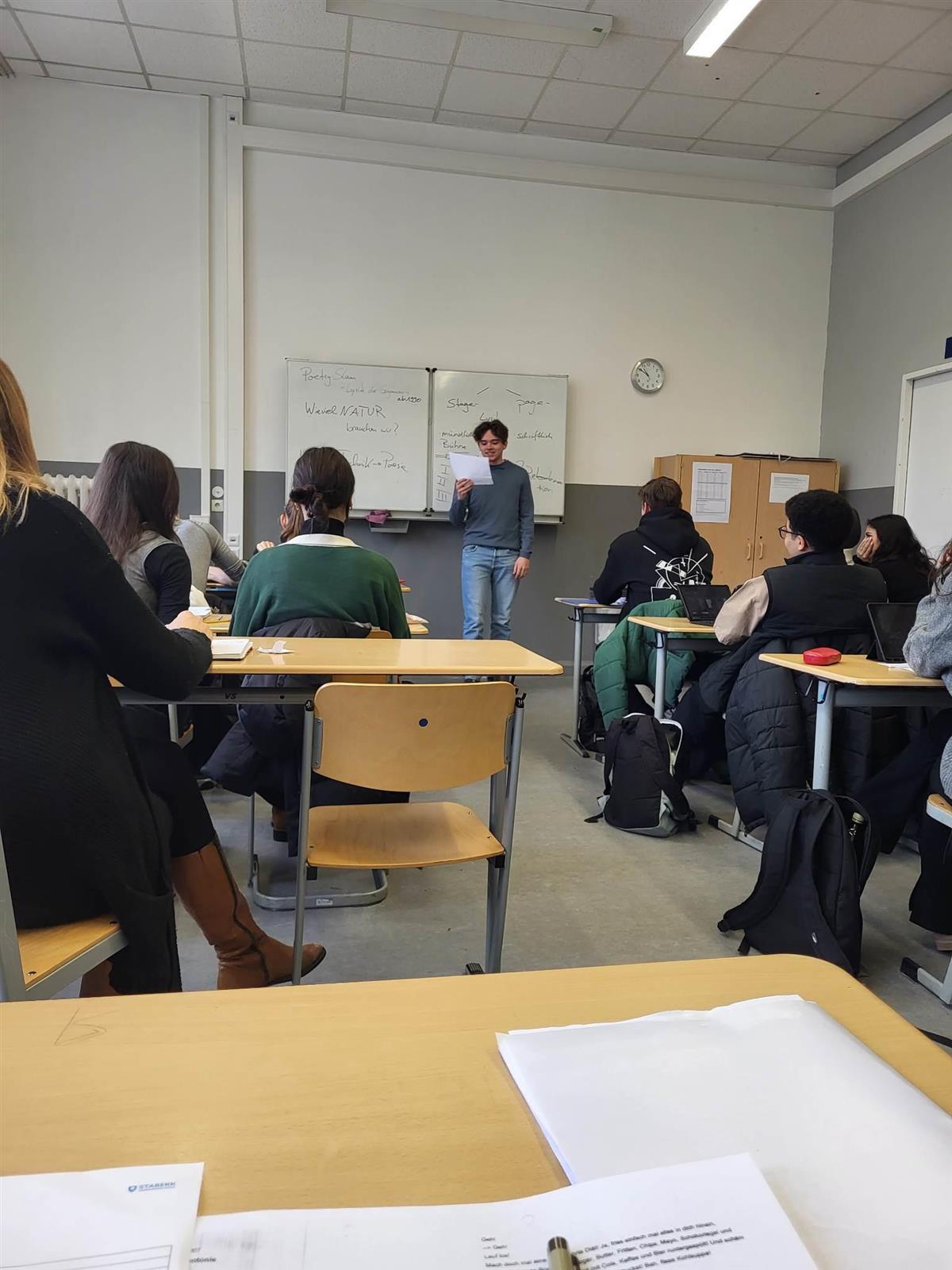 Elever sitter på pulter i et klasserom med lærer foran ved tavlen - Klikk for stort bilde