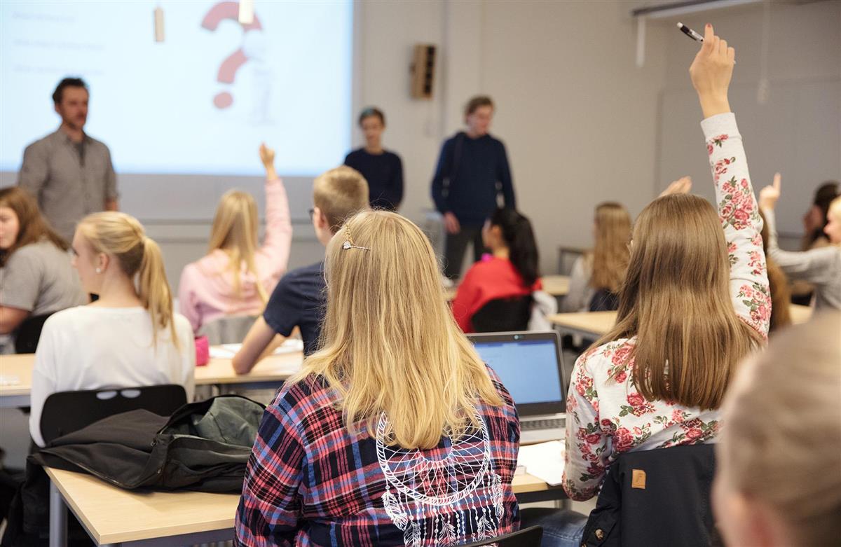 Elever i et klasserom som rekker opp hendene - Klikk for stort bilde