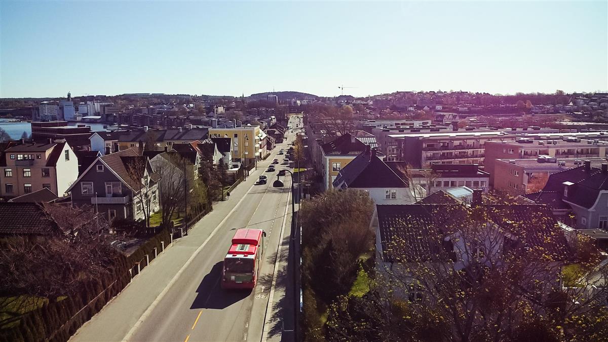 Rød buss kjører på vei gjennom boligområde - Klikk for stort bilde