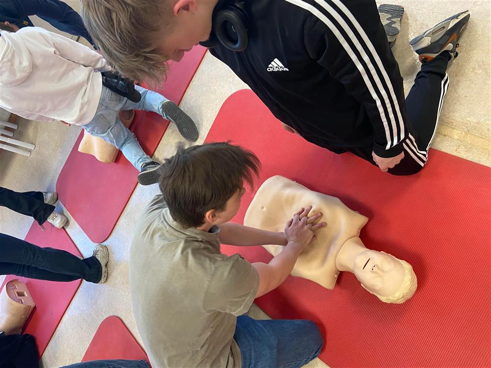 To elever utøver førstehjelp på en dukke på gulvet - Klikk for stort bilde