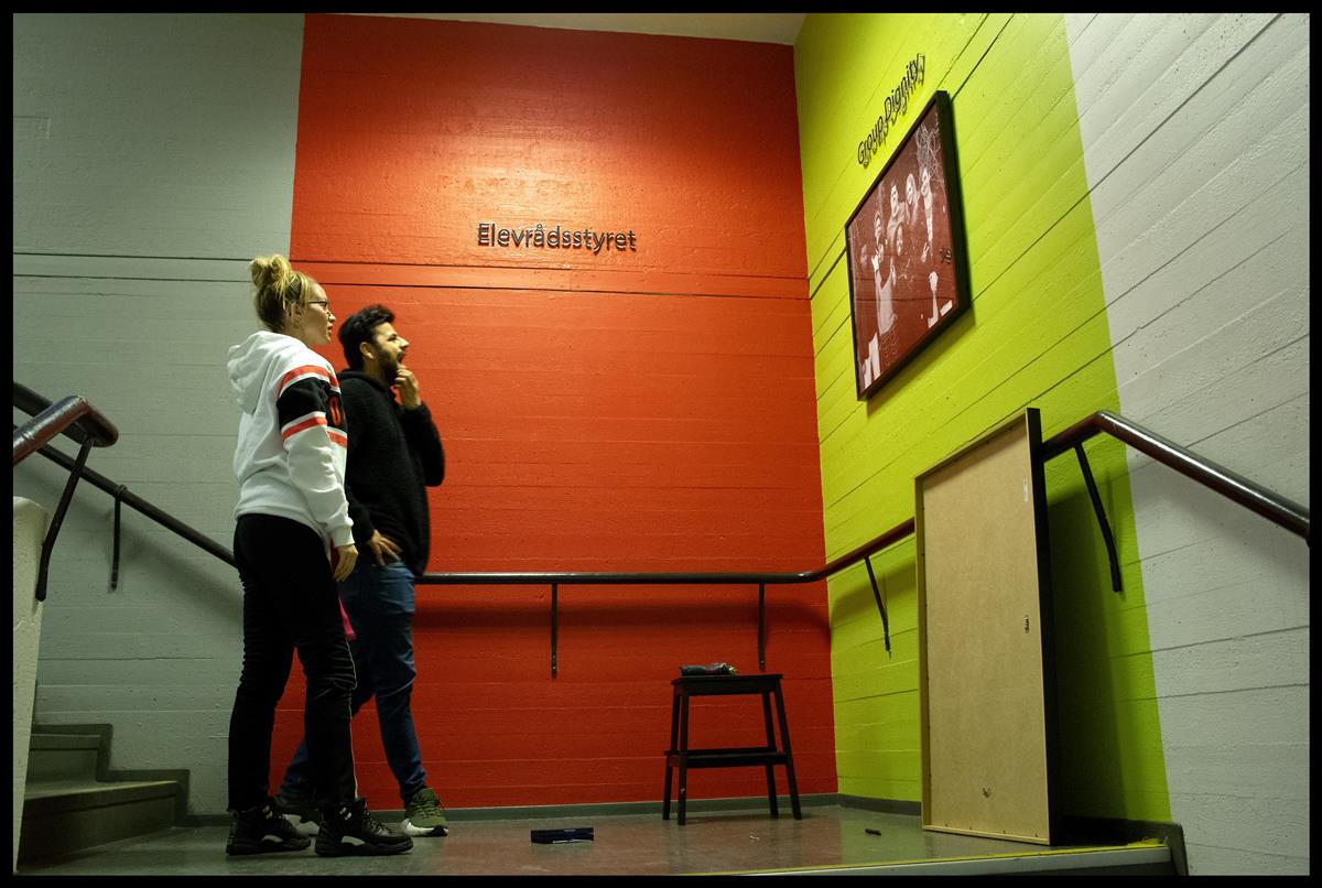 Miljøarbeiderne, Mira og Shahsawar, henger opp bilder av elevrådet i trappa - Klikk for stort bilde