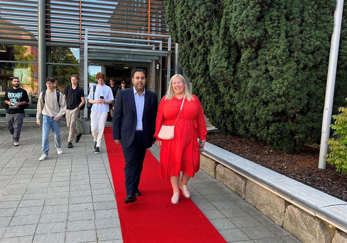Masud Gharahkhani og Heidi Westbye Nyhus går på rød løper. I bakgrunnen skimtes skolebygget og elever - Klikk for stort bilde