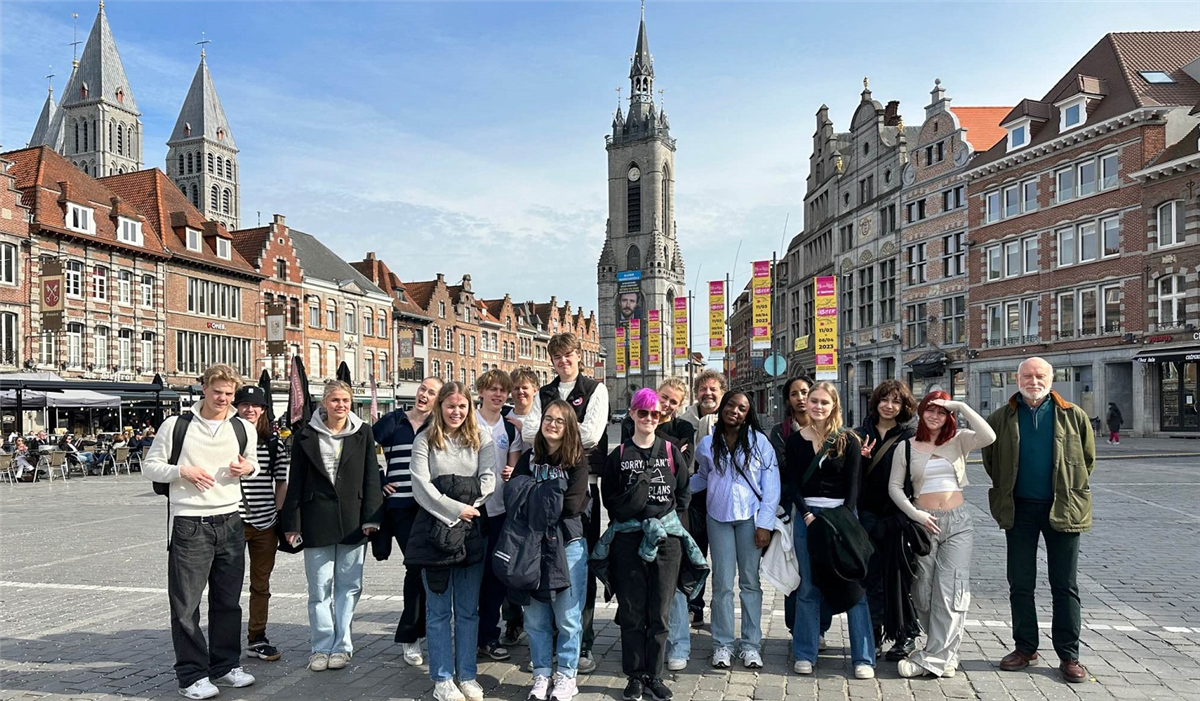 Bildet viser en gruppe mennesker som står oppstilt på et brosteinslagt torg i en by i Belgia. - Klikk for stort bilde